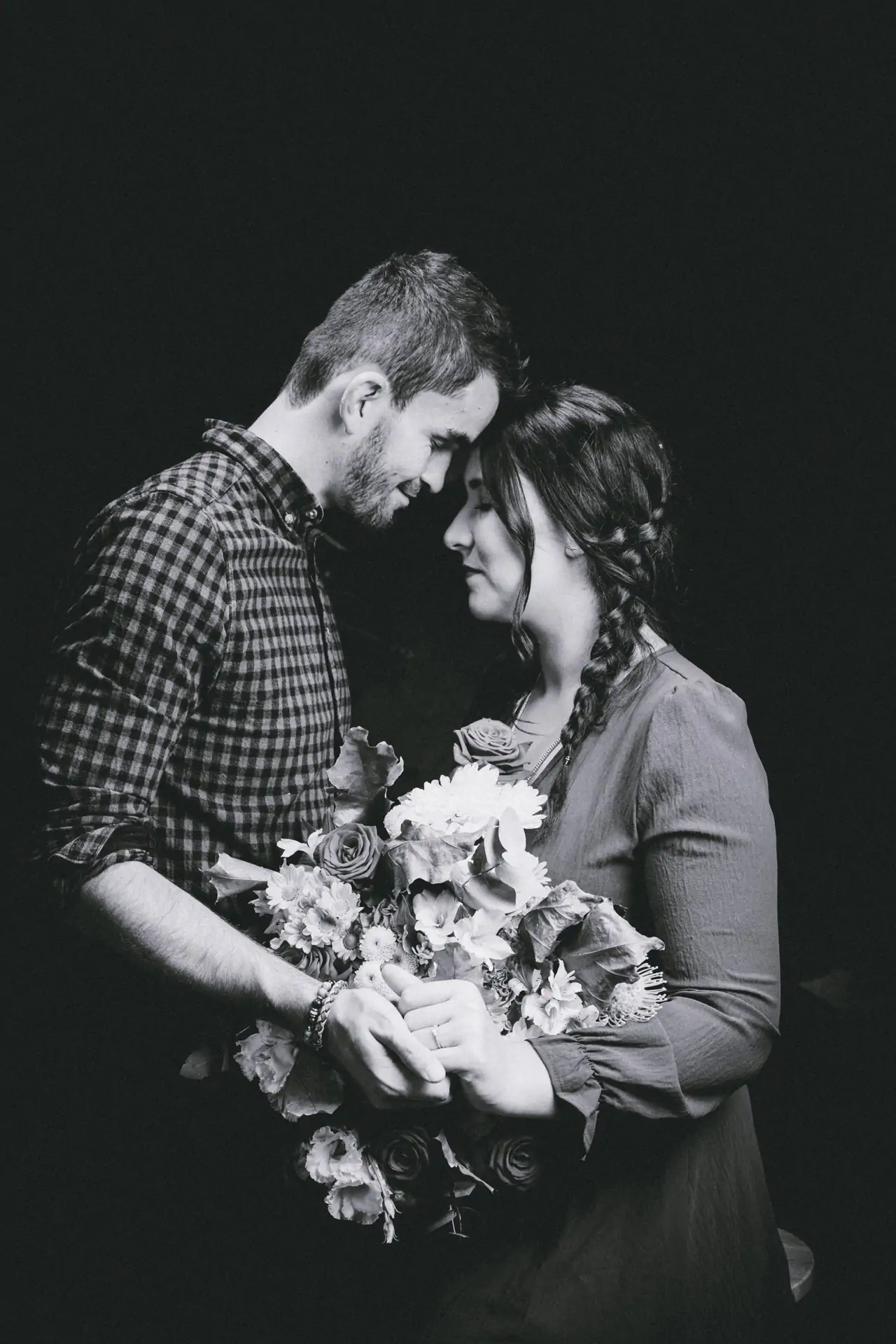 Portrait d'un couple avec un gros bouquet de fleur en noir et blanc dans un studio de photographie