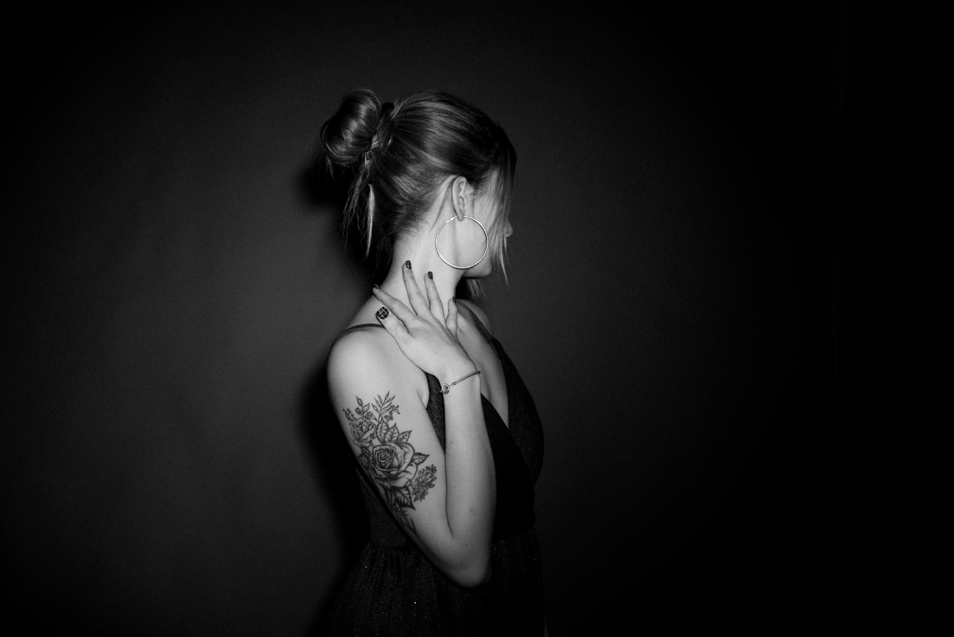 femme de profil avec une robe de soirée et des tatouages les cheveux attachée photo noir et blanc en studio