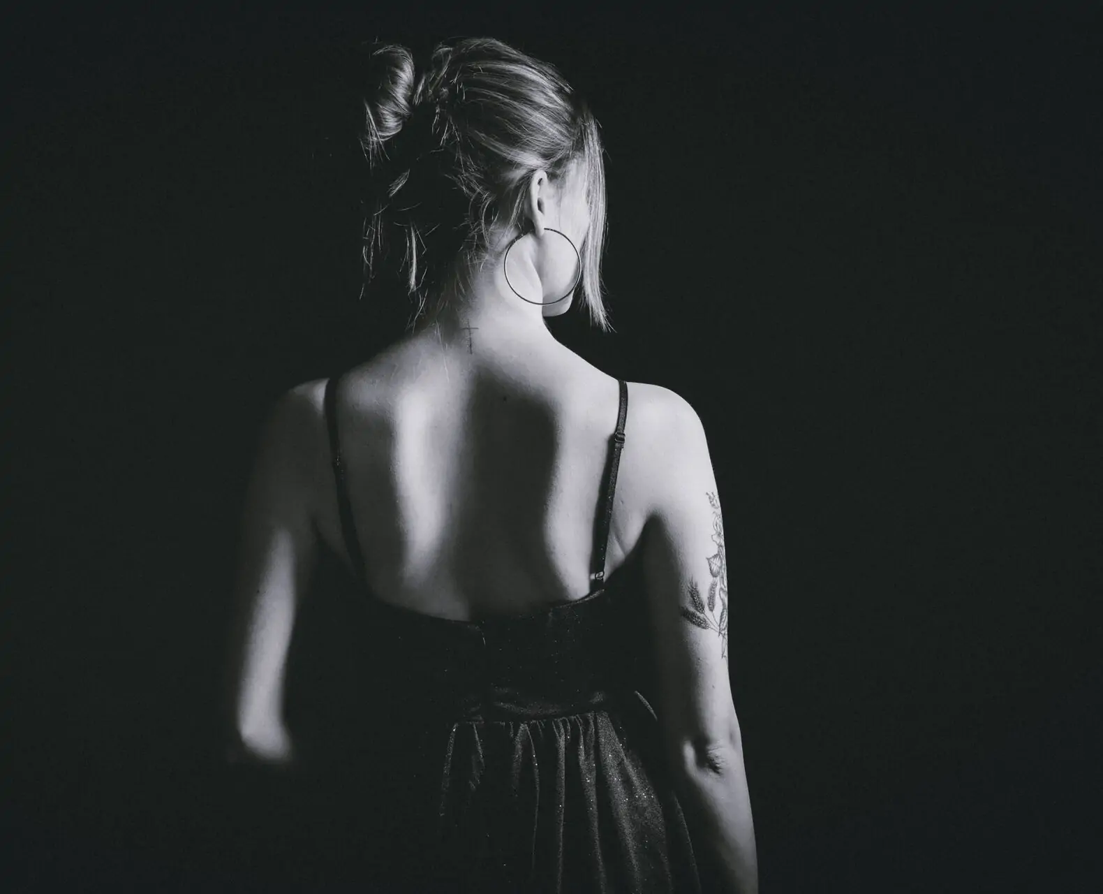 femme de dos avec une robe de soirée et des tatouages les cheveux attachée en chignon photo noir et blanc en studio