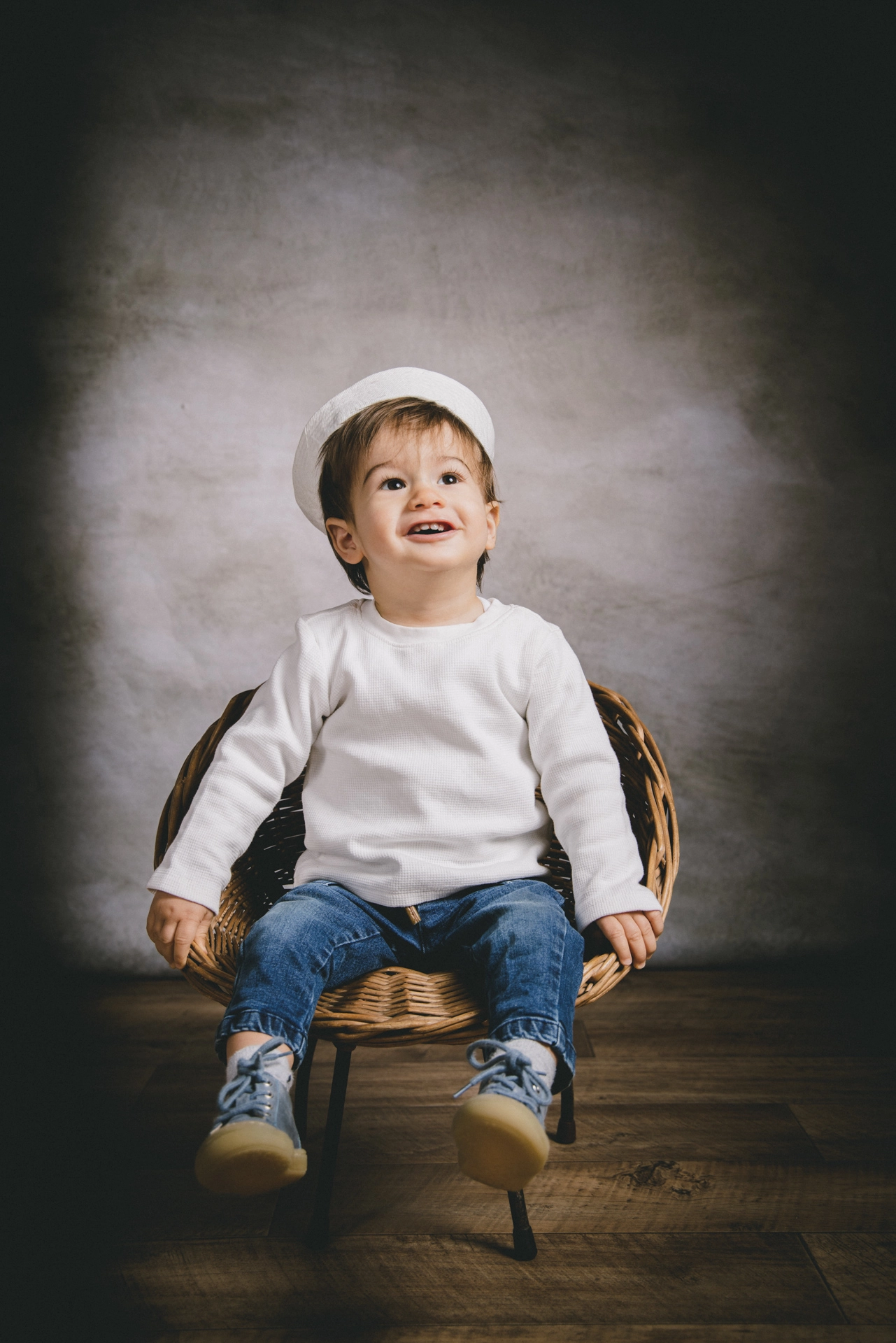 petit garçon en studio de photographie que regarde en l'air il est assis dans un petit fauteuil en rotin