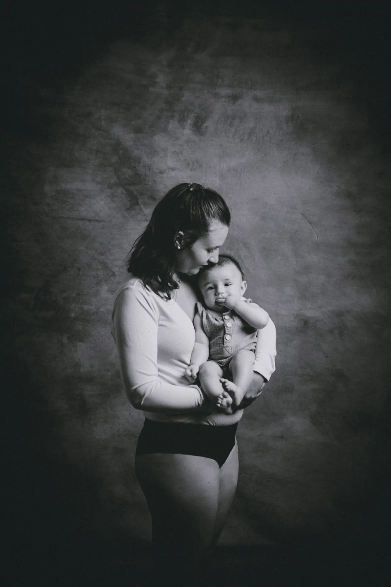 photo en noir et blanc d'une jeune maman en body qui fait un câlin à son bébé en studio de photographie