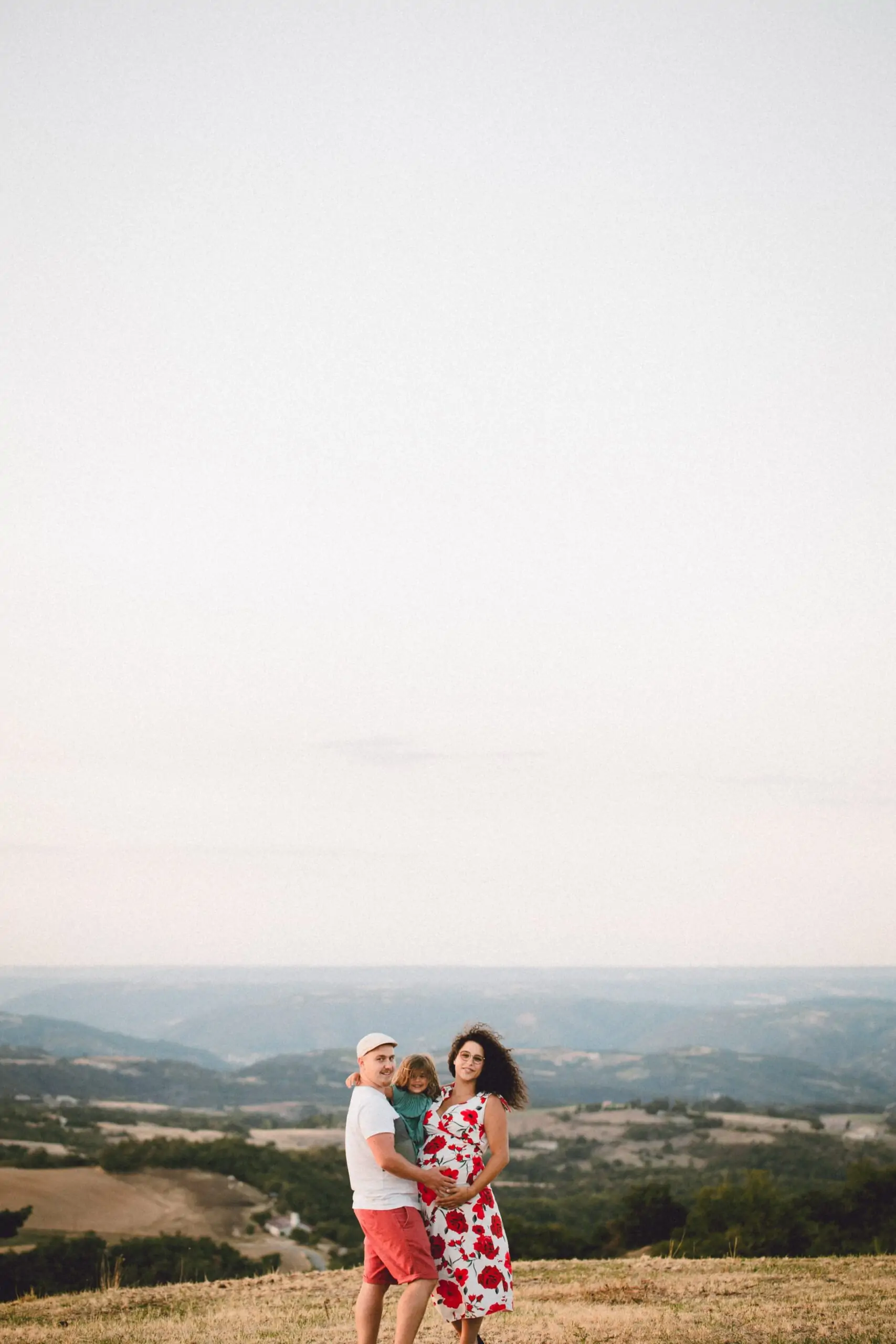 famille femme enceinte au coucher du soleil sur une colline avec une robe a fleurs rouges