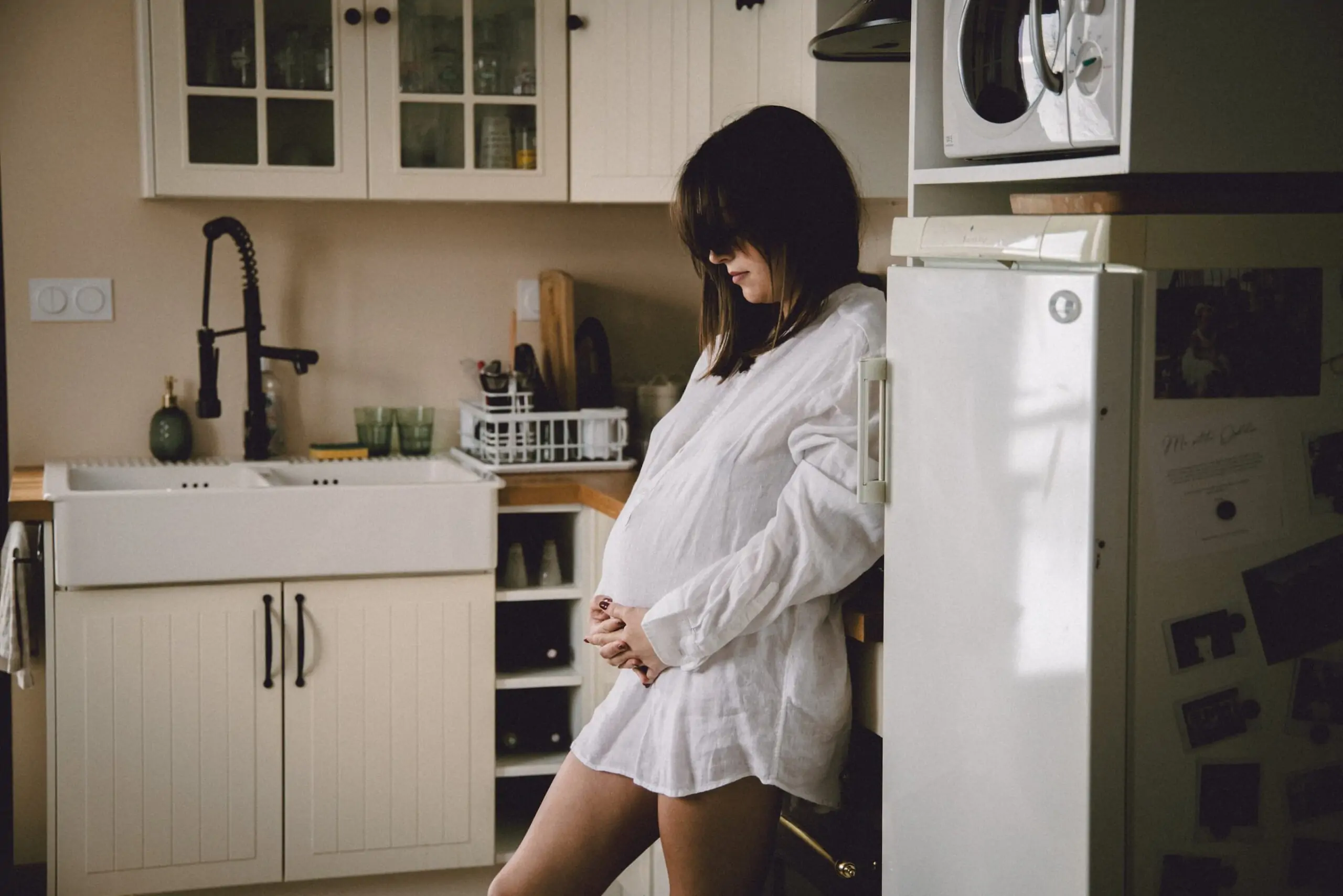 maman qui attend un bébé dans la cuisine en chemise blanche