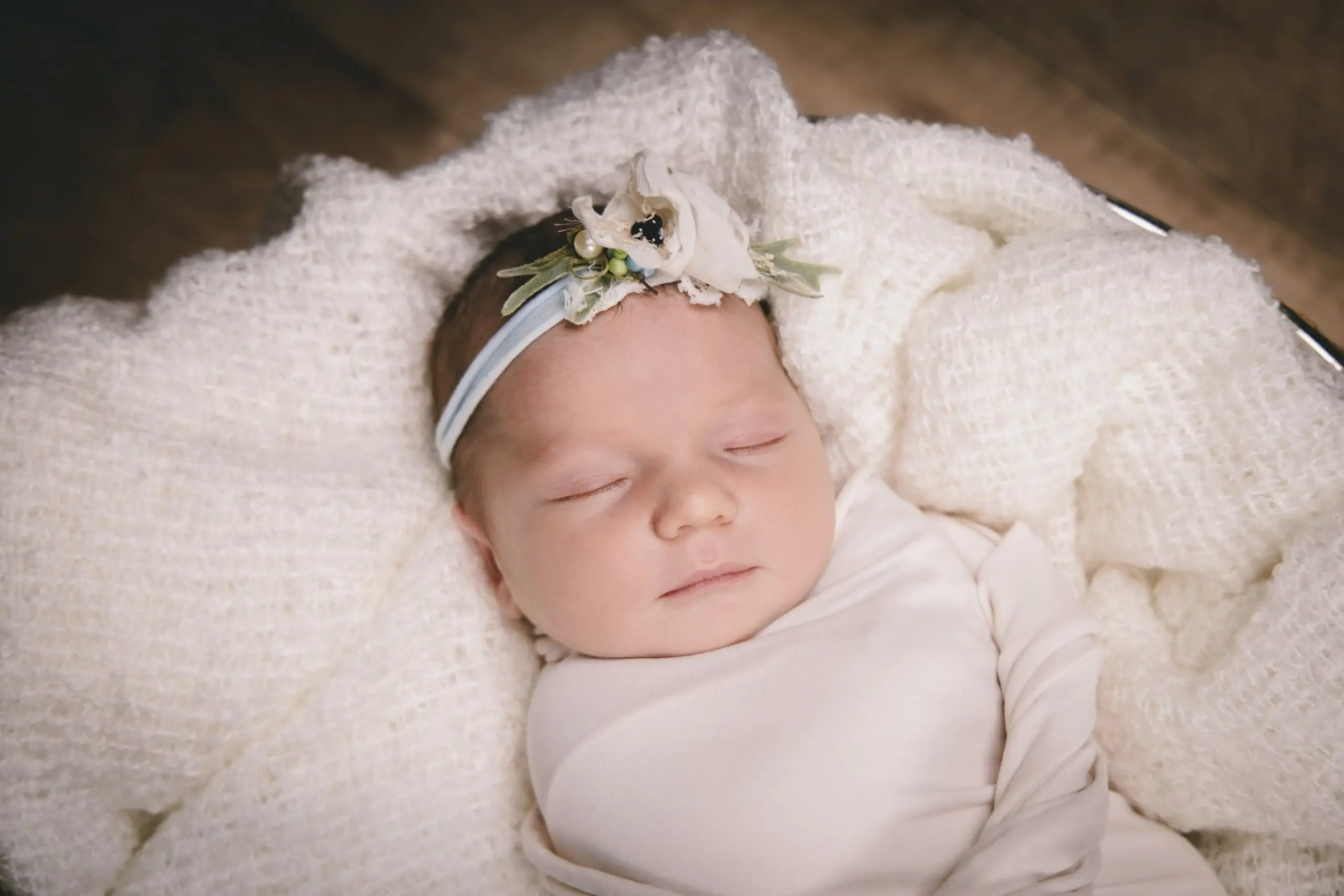 nouveau né emmailloté qui dort dans une couverture blanche elle porte un bandeau avec ds fleurs