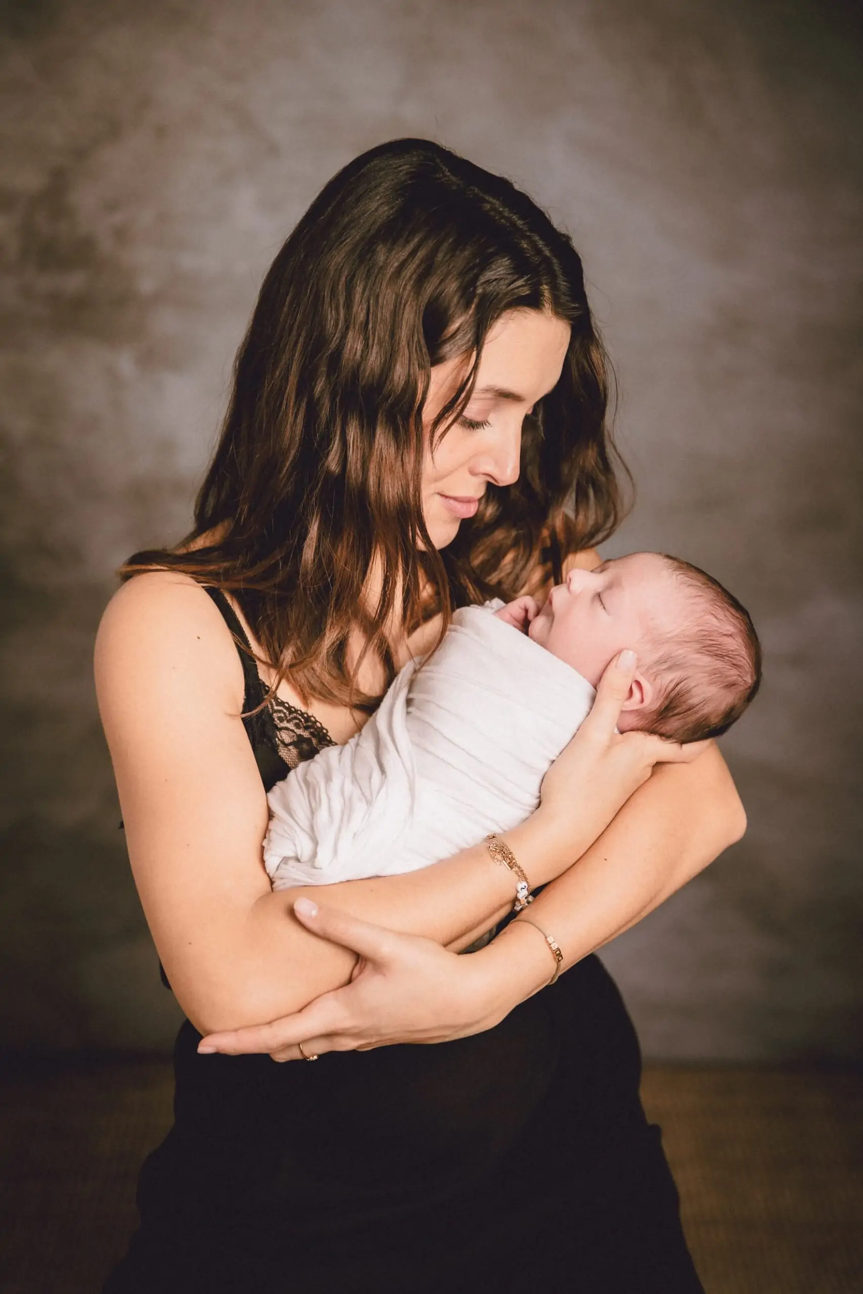 jeune maman qui porte son bébé nouveau né dans ses bras elle le regarde avec amour