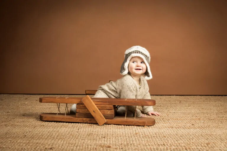 bebe aviateur sur un avion en bois il porte un bonnet en crochet qui représente un casque d'aviateur en studio de photographie Annonay